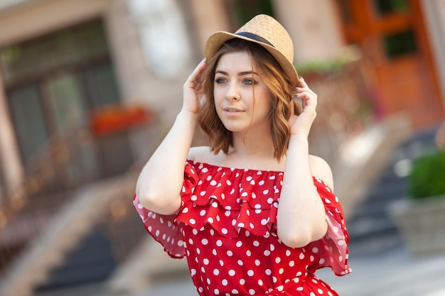 Portrait of a beautiful woman in a red polka dot dress and hat in the city