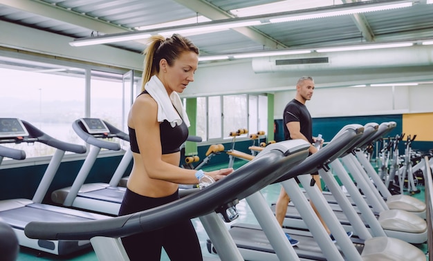 Portrait of beautiful woman setting control panel of treadmill for training in fitness center. Sport and technology concept.