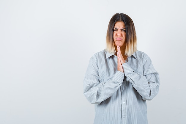 Ritratto di bella donna che mostra le mani giunte in un gesto di supplica in camicia e sembra felice vista frontale