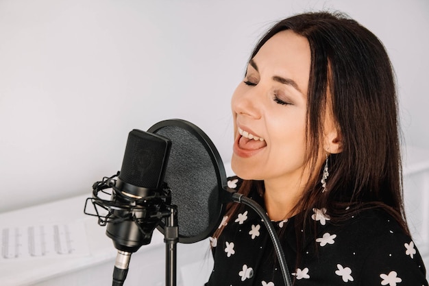 Портрет красивой женщины поет песню возле микрофона в студии звукозаписи