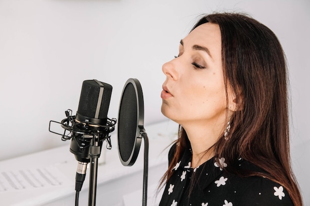 Portrait of beautiful woman sings a song near a microphone in a recording studio