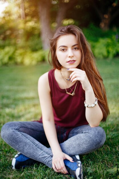 Photo portrait of beautiful woman sitting on grassy land in park