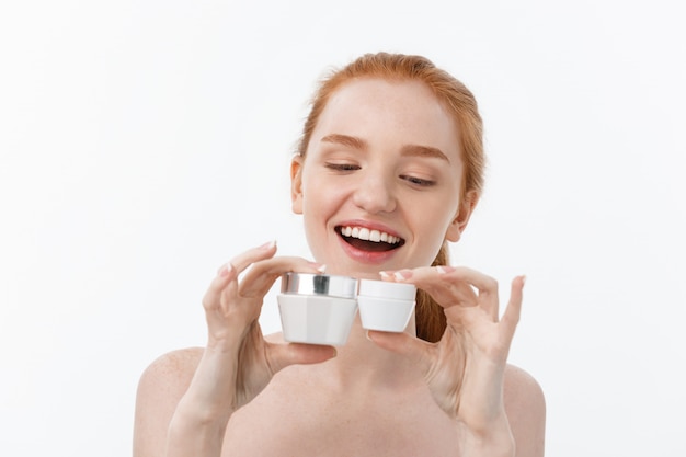 Photo portrait of beautiful woman smiling while taking some facial cream isolated on white background with copy space.