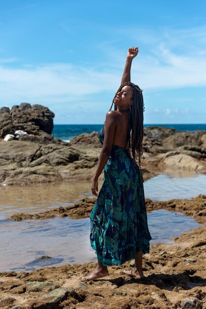 Foto ritratto di una bella donna in piedi con gli abiti blu in cima alle rocce sulla spiaggia