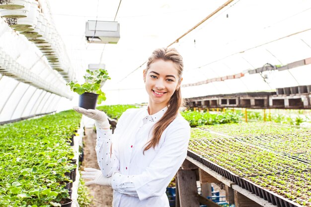 Portrait of a beautiful woman standing in a white dressing gown and holding a small pot with plant in her hand