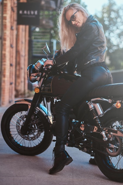 Photo portrait of beautiful woman in sunglasses and leather clothing on the motorbike.