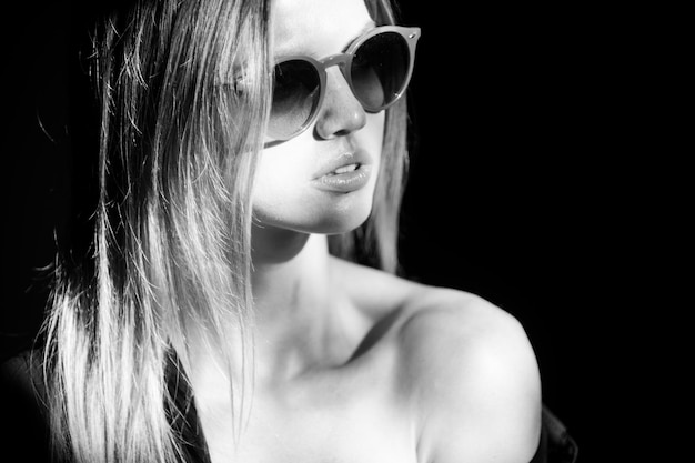 Portrait of beautiful woman in sunglasses model looking seductive and sensual. Beauty face with dramatic studio light isolated on black.