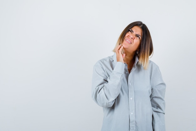 Portrait of beautiful woman touching chin while looking up in shirt and looking confused front view