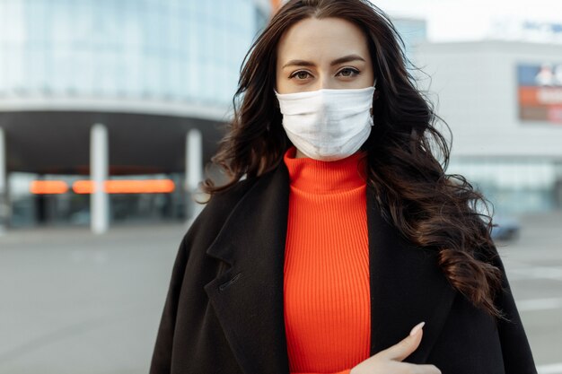 Portrait of beautiful woman walking on the street wearing protective mask as protection against infectious diseases. Attractive unhappy model with flu outdoors