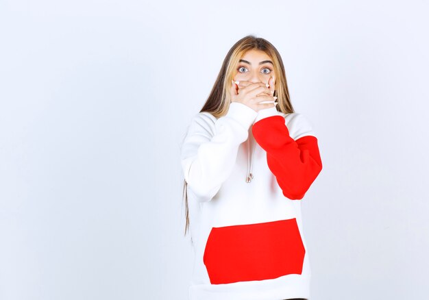 Portrait of a beautiful woman in warm hoodie standing and covering mouth with hands 