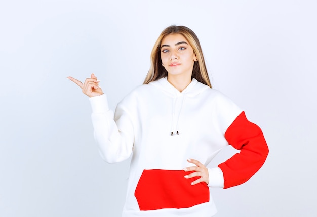 Portrait of a beautiful woman in warm hoodie standing and pointing away