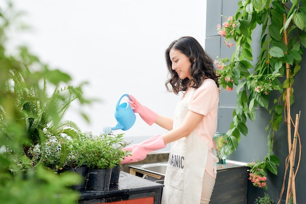 バルコニー、アパートの小さな居心地の良い庭で緑の植物に水をまく美しい女性の肖像画