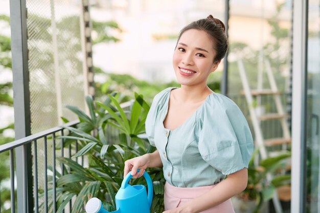 アパートのバルコニーの小さな居心地の良い庭で緑の植物に水をまく美しい女性の肖像画