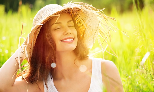 Portrait of beautiful woman wearing straw hat with large brim at beach and looking at camera.