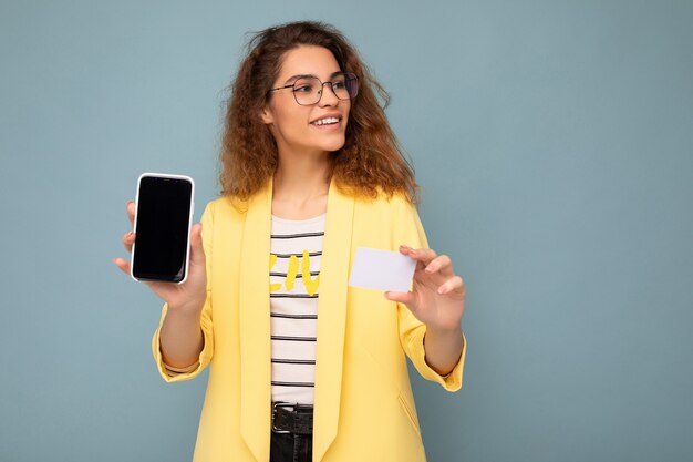 Portrait of beautiful woman wearing yellow jacket and optical glasses isolated on background wall