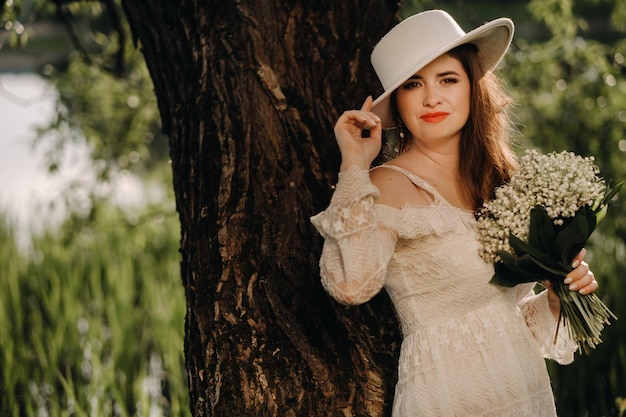 Portrait of a beautiful woman in a white dress and a hat with lilies of the valley A girl in nature Spring flowers