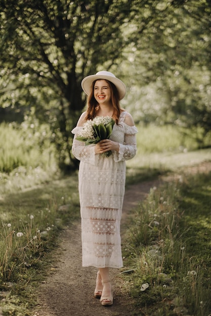 Portrait of a beautiful woman in a white dress and a hat with lilies of the valley a girl in nature