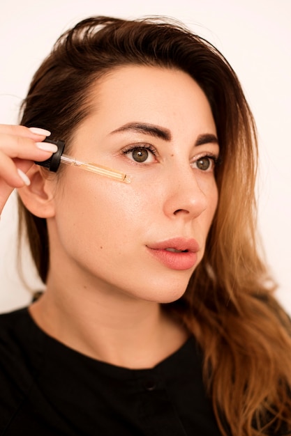 Portrait of a beautiful woman who moisturizes her skin. She brings it to her face and then rubs it into the skin