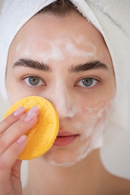 Photo portrait of beautiful woman with clear skin washing face with foam cleanser and sponge