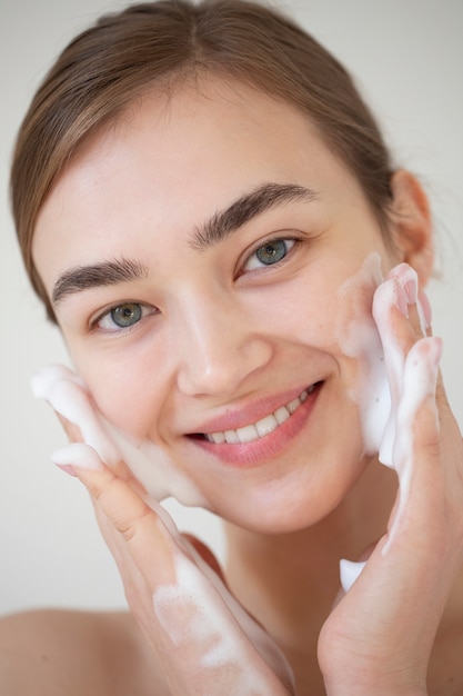 Photo portrait of beautiful woman with clear skin washing face with foam cleanser