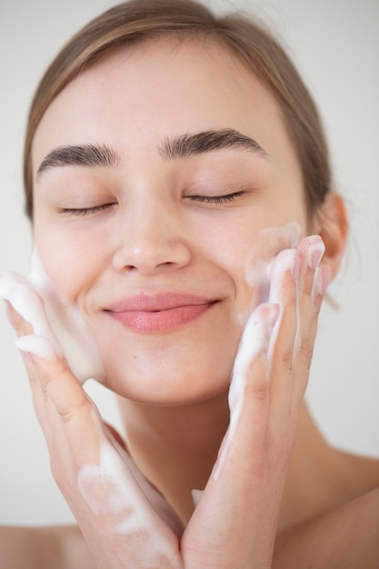 Photo portrait of beautiful woman with clear skin washing face with foam cleanser