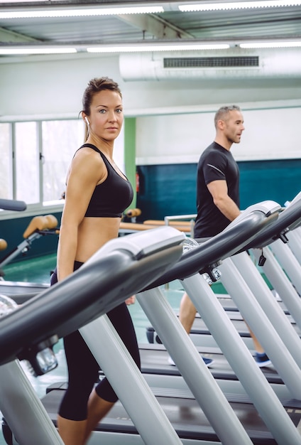 Portrait of beautiful woman with earphones training over a treadmill on fitness center.