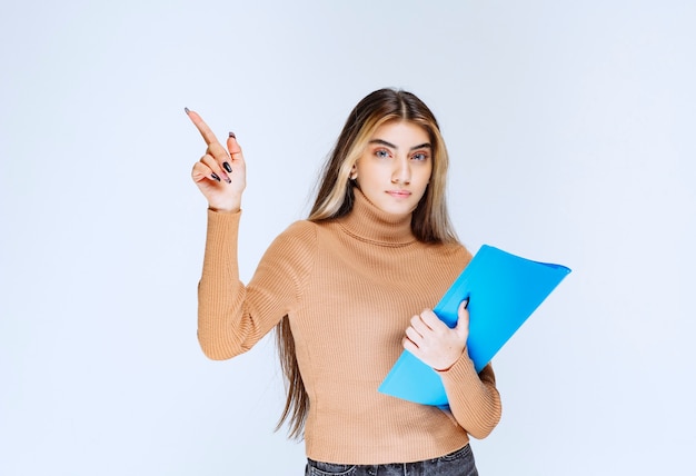 Portrait of a beautiful woman with a folder standing and pointing up .