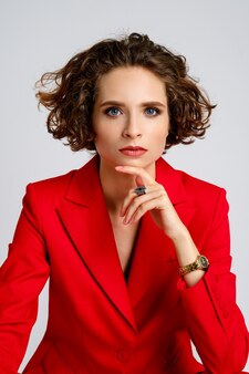 Ritratto di bella donna con trucco naturale, capelli corti ricci e giacca rossa che puntella il mento
