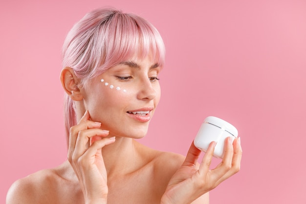 Portrait of beautiful woman with pink hair and face cream applied on her skin like dots holding and