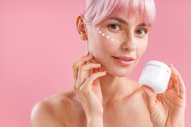 Portrait of beautiful woman with pink hair and face cream applied on her skin like dots looking at