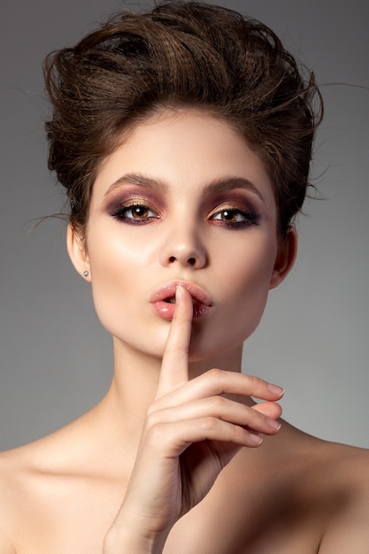 Portrait of beautiful woman with romantic red and gold smokey eyes makeup showing shh sign
