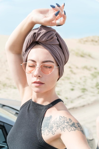 Portrait of a beautiful woman with a tattoo in sunglasses and turban on a desert background