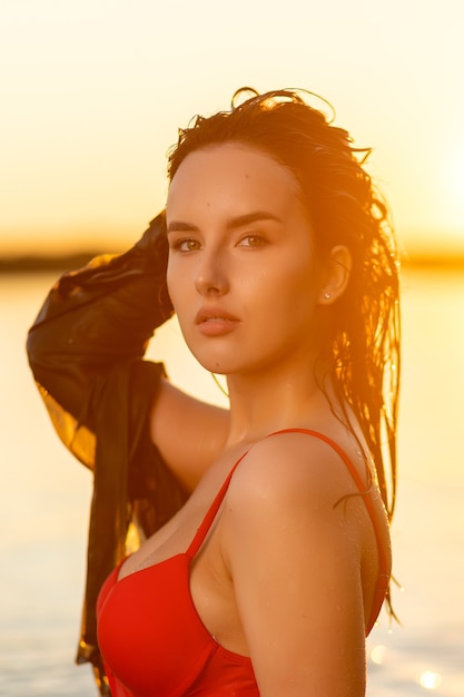 Portrait of a beautiful woman with wet hair in a sexy red bikini against the backdrop of the sea and sunset. fashionable stylish young woman on tropical beach