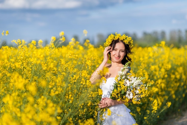 Portrait of a beautiful woman with a wreath of yellow flowers on her head A girl with a bouquet in a rapeseed field