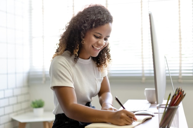 Foto ritratto di giovane e bella donna africana sorridente che lavora sul desktop mentre era seduto in un ufficio moderno