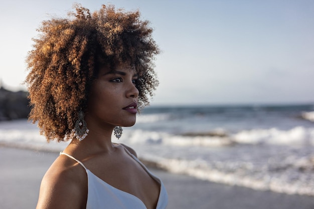 Portrait of beautiful young African woman in white dress with beach background