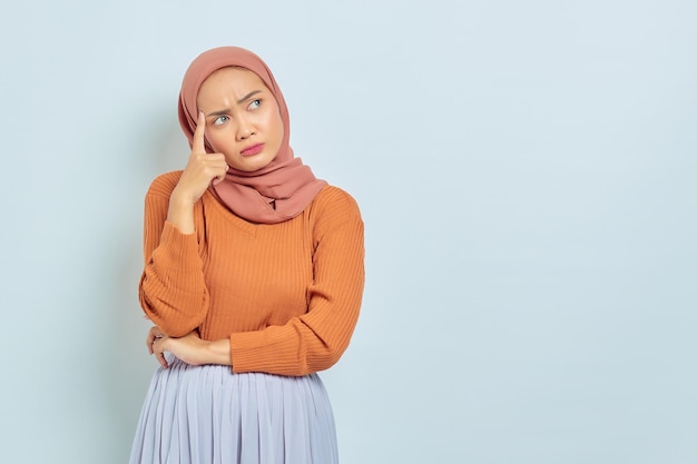 Portrait of beautiful young Asian Muslim woman in brown sweater looking serious thinking about question and looking at copy space isolated on white background Muslim lifestyle concept