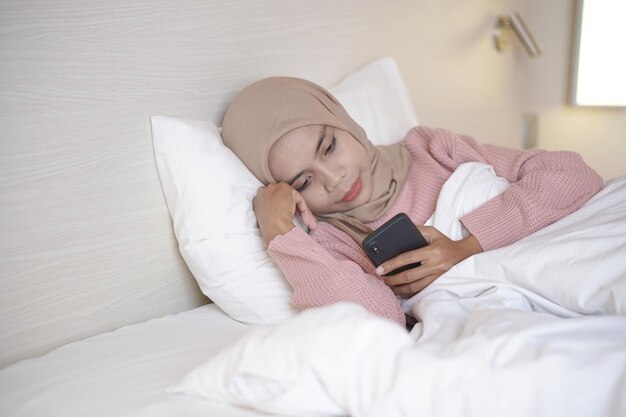 침대에 누워 자는 동안 머리 스카프를 착용하고 있는 아름다운 젊은 아시아 무슬림 여성의 초상화