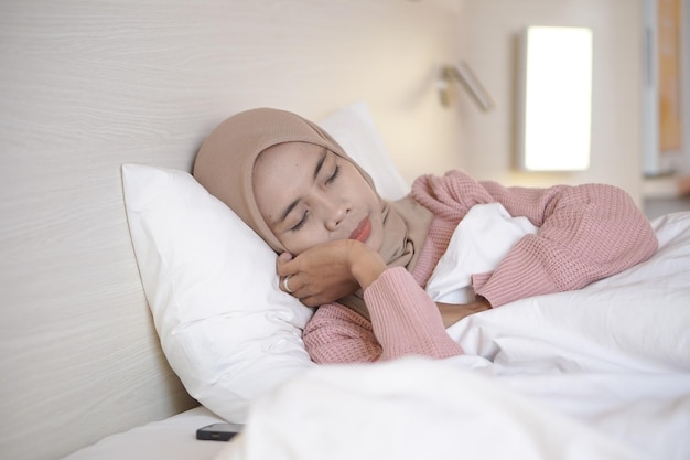 Portrait of a beautiful young Asian Muslim woman wearing a headscarf while lying in bed and sleeping