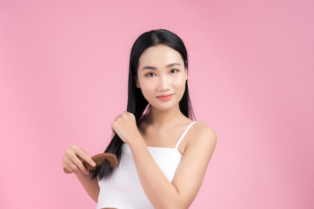 Portrait of beautiful young Asian woman combing her hair, looking at camera and smiling