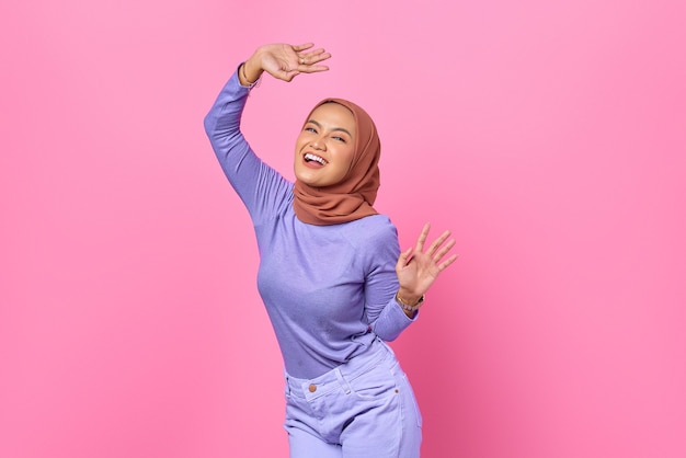 Portrait of beautiful young Asian woman dancing happy and cheerful on pink background