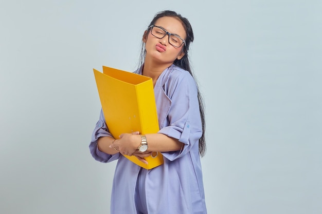 Portrait of beautiful young Asian woman hugging yellow folder and giving kiss isolated on purple background