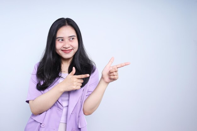 Portrait of beautiful young Asian woman pointing to the side over grey background