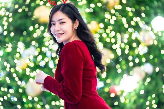 Portrait beautiful young asian woman red dress costume and Christmas greeting picture parcel decoration on Christmas tree light circular bokeh background Decoration During Christmas and New Year.