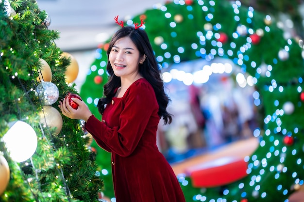 肖像画の美しい若いアジアの女性の赤いドレスの衣装とクリスマスツリーのクリスマスの挨拶の絵の小包の装飾明るい円形のボケの背景クリスマスと新年の装飾。