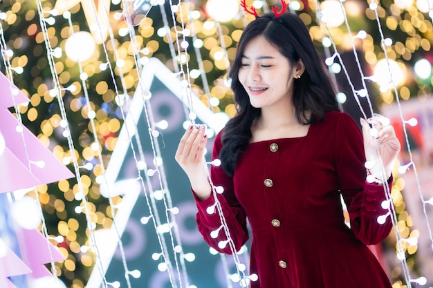 Portrait beautiful young asian woman red dress costume and Christmas greeting picture parcel decoration on Christmas tree light circular bokeh background Decoration During Christmas and New Year.