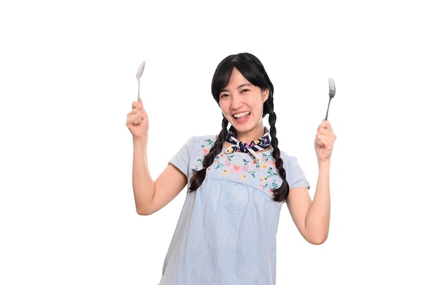 Портрет красивой молодой азиатской женщины улыбается в джинсовом платье с ложкой и вилкой на белом фоне
