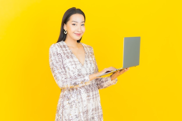 Portrait beautiful young asian woman smile with computer laptop on yellow