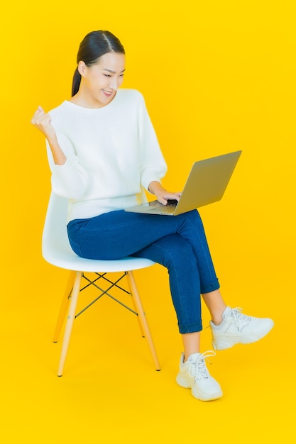 Portrait beautiful young asian woman smile with computer laptop on yellow