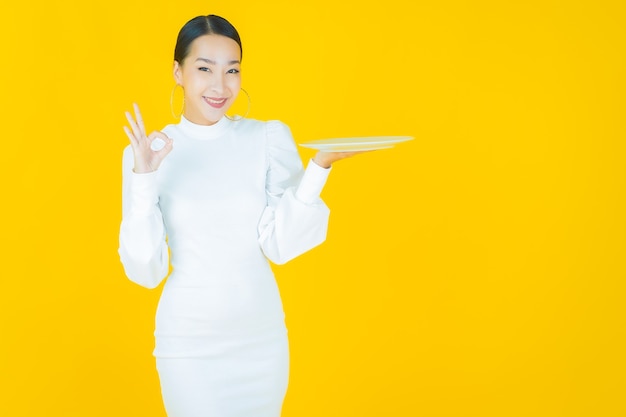 Portrait beautiful young asian woman smile with empty plate dish on yellow